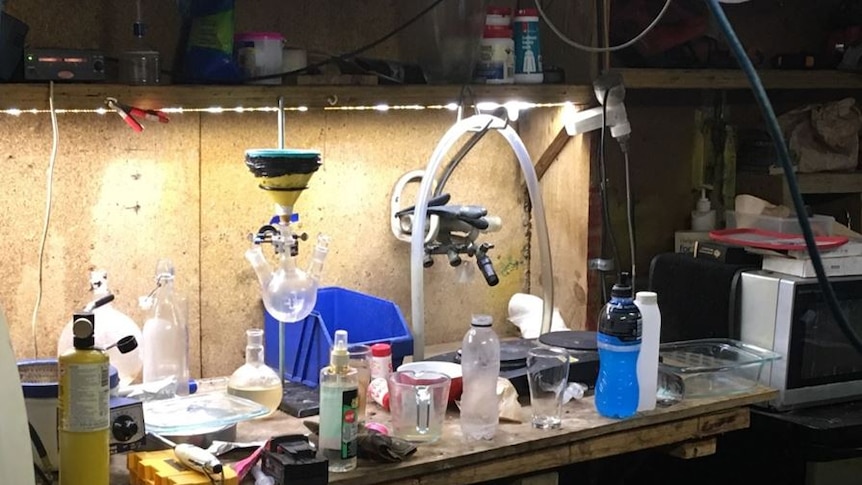 The bench of a meth lab, with bottles and beakers and a microwave.