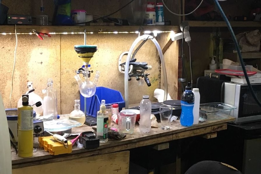 The bench of a meth lab, with bottles and beakers and a microwave.