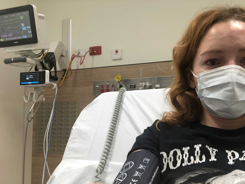 Selfie of Georgia Mooney wearing mask and black Dolly Parton t-shirt sitting in a bed at St Vincent's Hospital