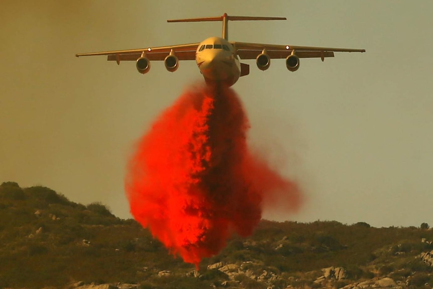 A water bomber drops retardant on a fire.