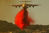 A water bomber drops retardant on a fire.