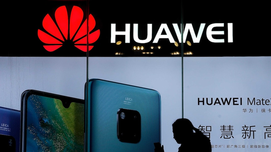 A woman browses her smartphone as she walks by a Huawei store.