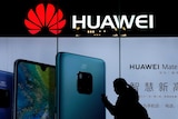 A woman browses her smartphone as she walks by a Huawei store.