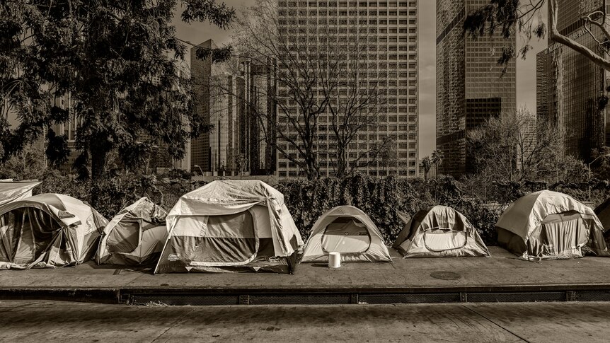 A row of homeless tents on a deserted urban street, with skyscrapers in the background