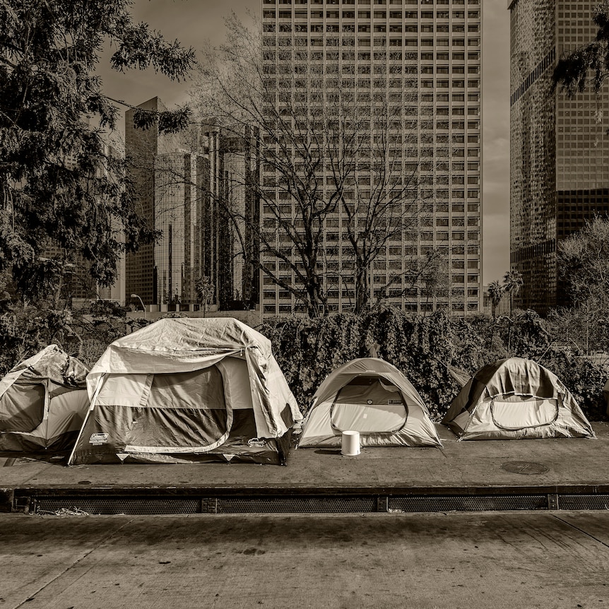 A row of homeless tents on a deserted urban street, with skyscrapers in the background