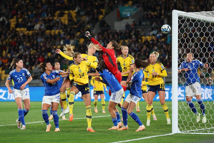 A tall Swedish player rises to head the ball past the goalkeeper into the Italian net.