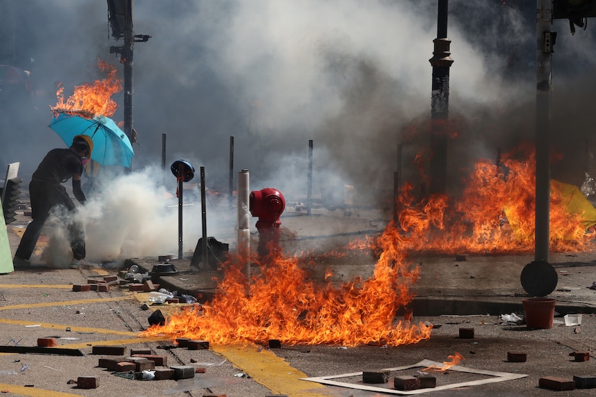 In streets lined with flames a protester's umbrella catches fire.