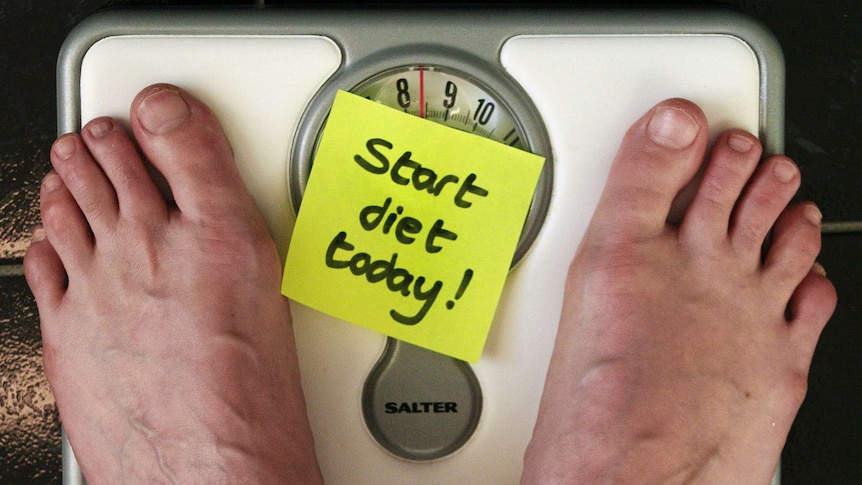 Feet on a set of scales with a sticky note reading 'start diet today'.