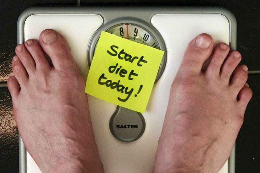 Feet on a set of scales with a sticky note reading 'start diet today'.