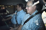 Dr Pridgeon sitting in a police car, looking straight ahead as camera crews try to get a shot of him through the car windows.