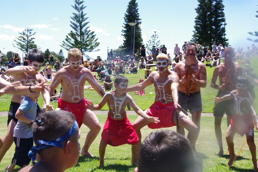 Men and boys in body paint performs traditional Indigenous dancing as a crowd looks on.