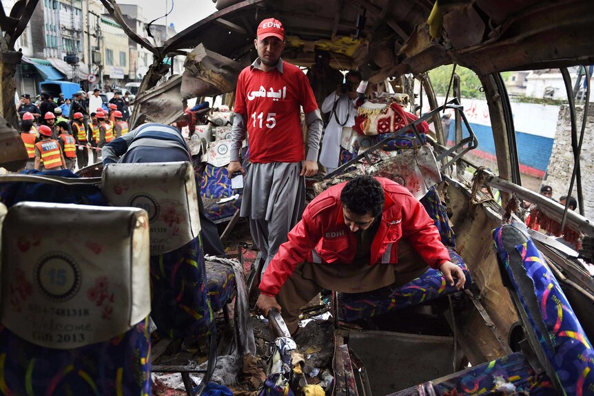 Pakistani volunteers search a bus damaged in a bomb blast