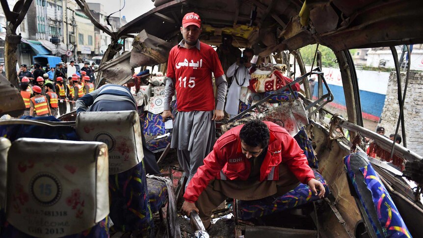 Pakistani volunteers search a bus damaged in a bomb blast