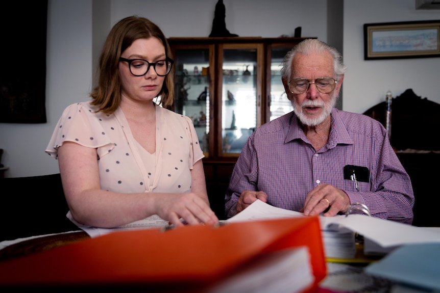 A woman and an older man look focused while sifting through binders full of documents.
