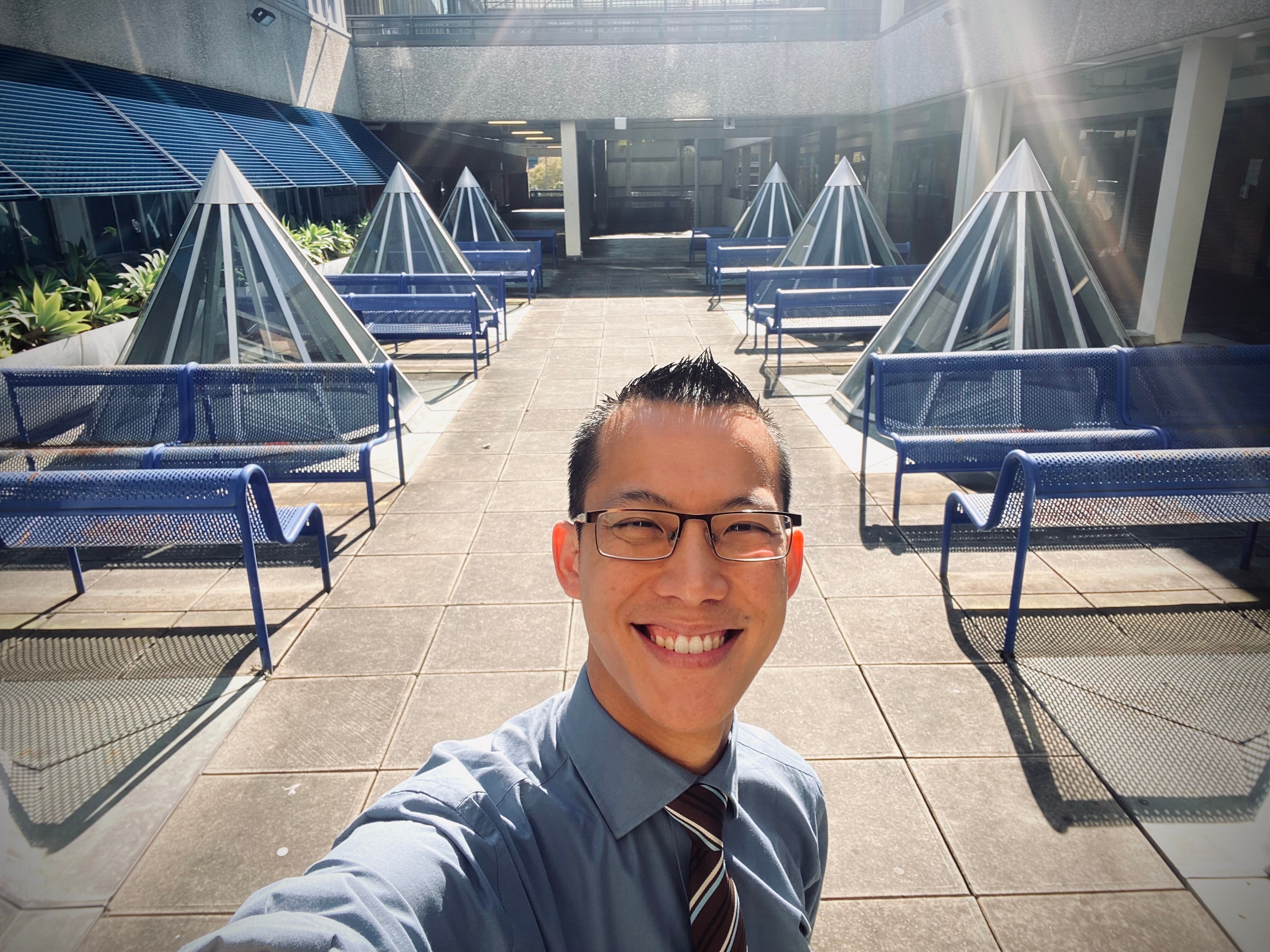 Maths teacher Eddie Woo smiles at the camera while taking a selfie outside while working.