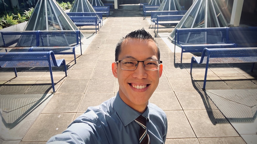 Maths teacher Eddie Woo smiles at the camera while taking a selfie outside while working.