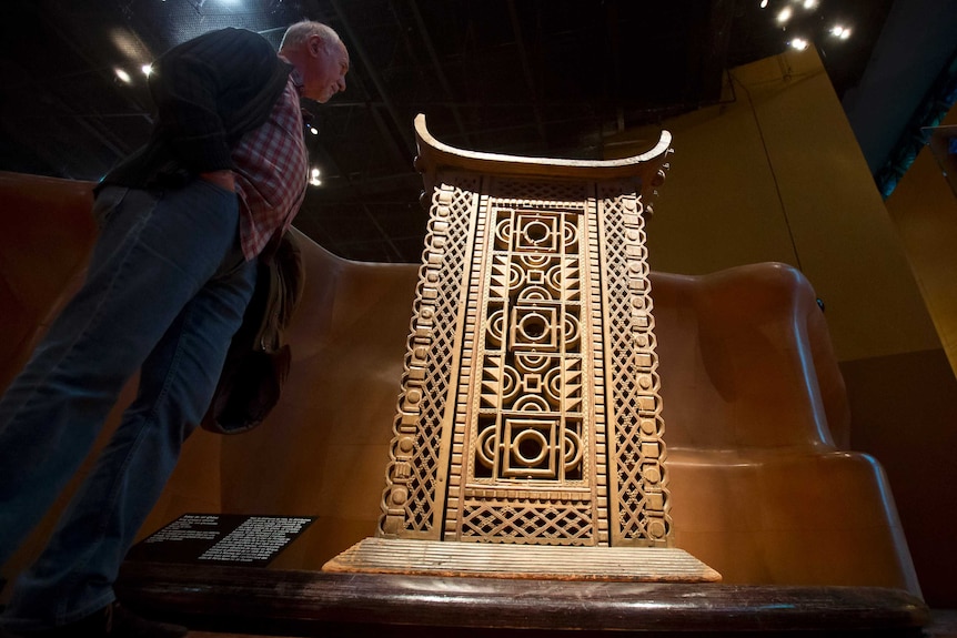 a man stands next to a wood and metal throne in a museum