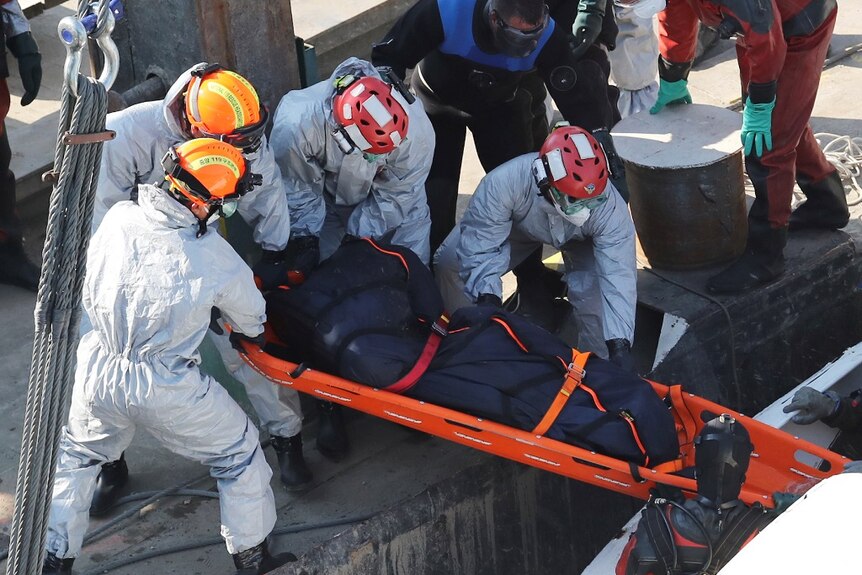 Crew members recover a body from the wreckage of a vessel that sunk in a river.