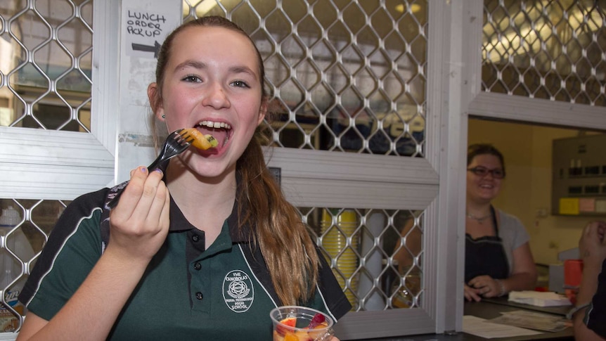 A girl in a school uniform with a fork to her mouth with fruit on it