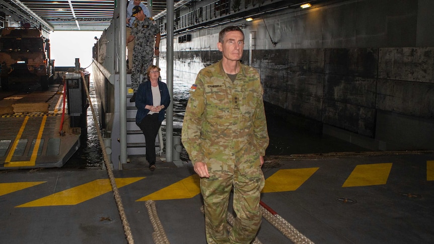 a man in uniform walks inside HMAS adelaide followed by a woman and two other men