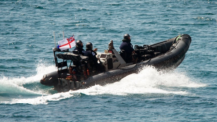 Three people in helmets and dark uniforms sail on a small inflatable boat.