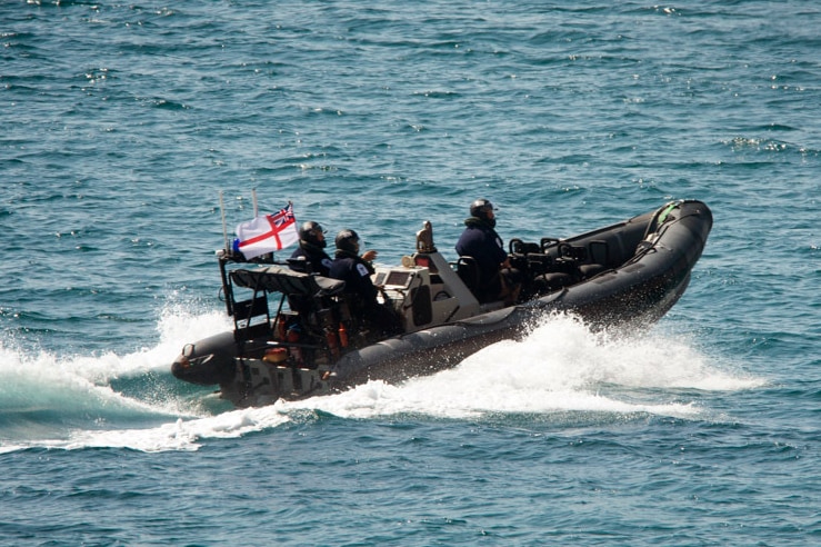 Three people in helmets and dark uniforms sail on a small inflatable boat.