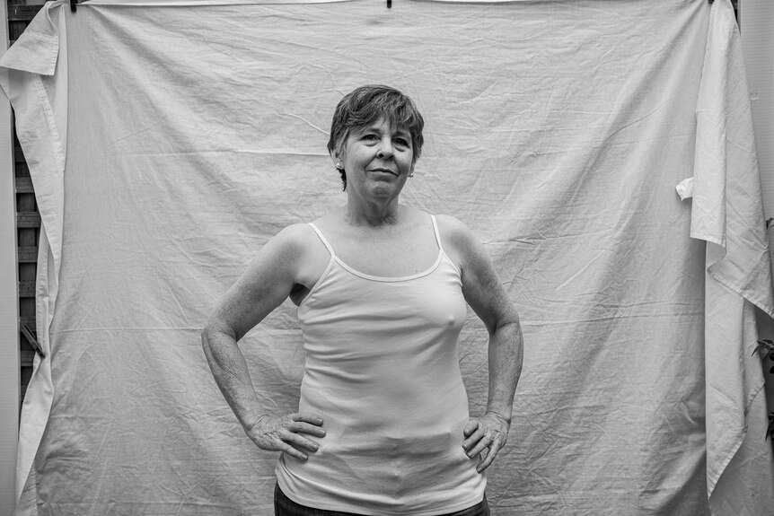 Rebecca Smyth stands with her hands on her hips in a white singlet that reveals she is living with just one breast.