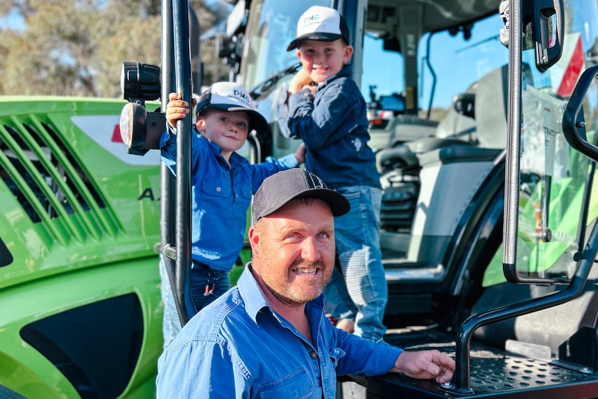 A man and two boys lean against a large green tractor
