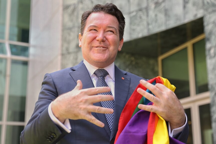 Dean Smith smiles while holding a rainbow flag.