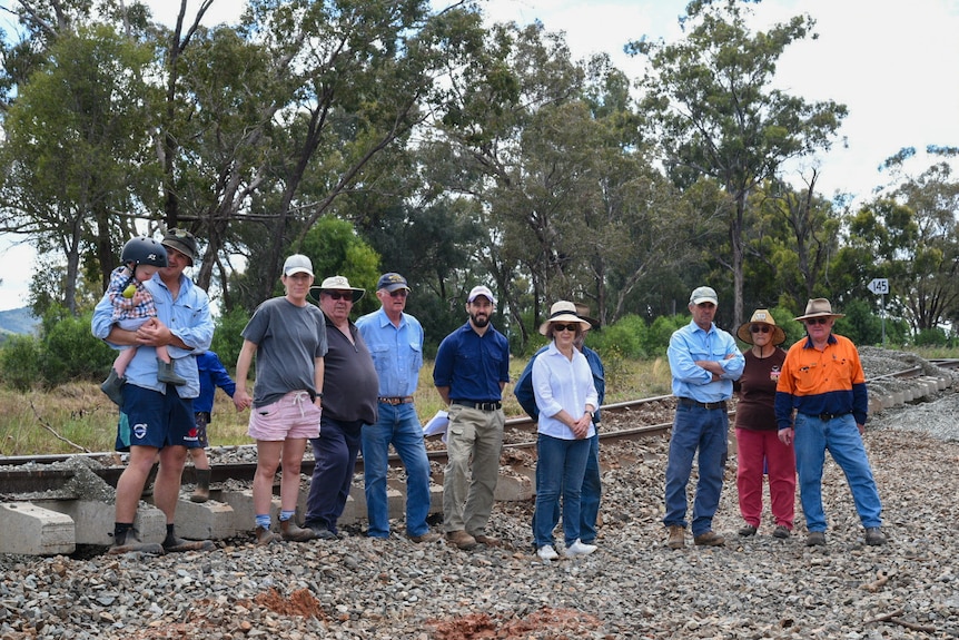 A group of people including small children standing in front of a damaged railway line.