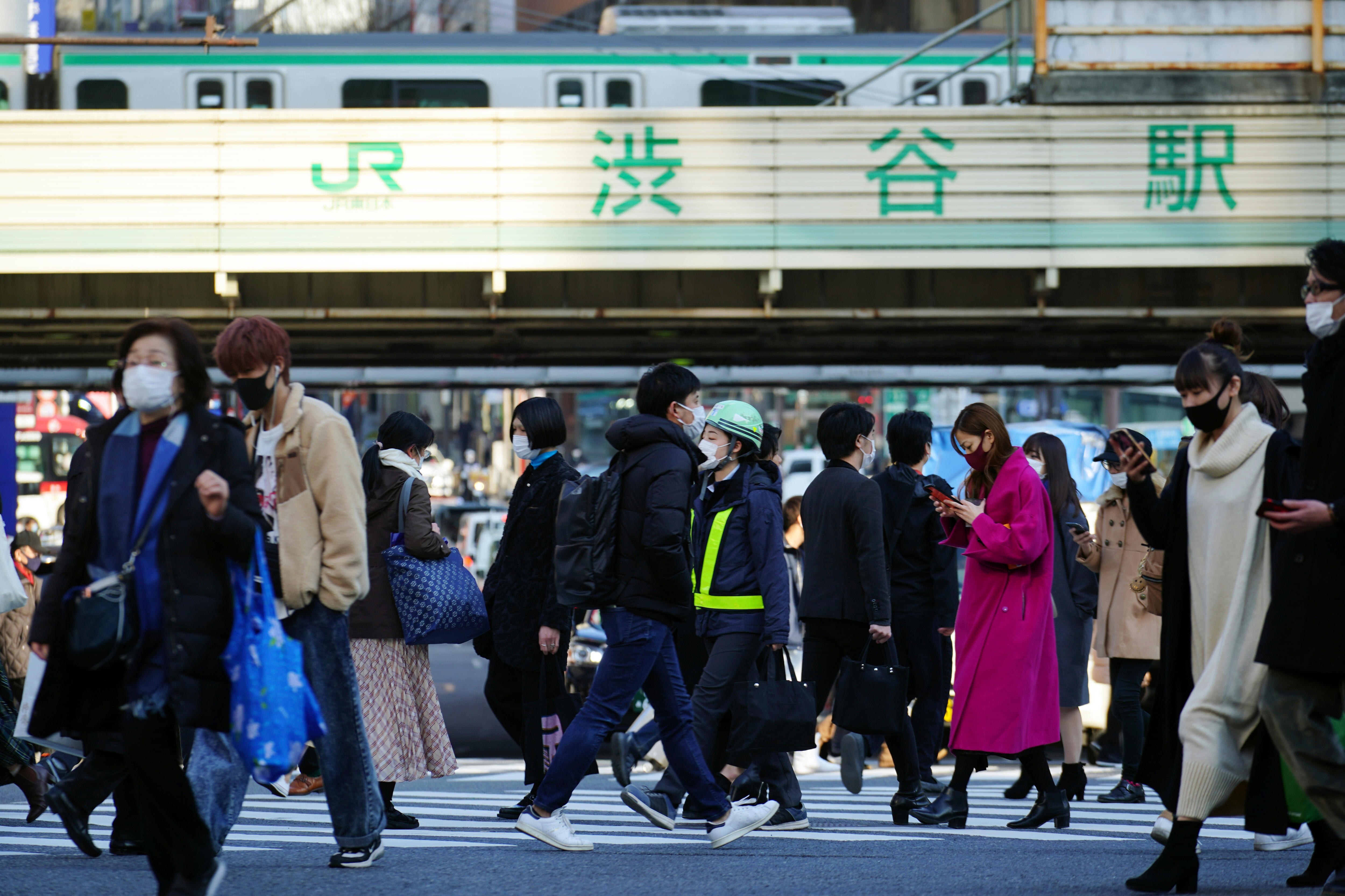 People wearing face masks are walking across the overpassing railway line in a busy area in Tokyo.