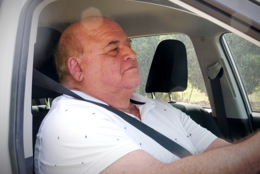 A man sits in the front seat of a car with a seatbelt on