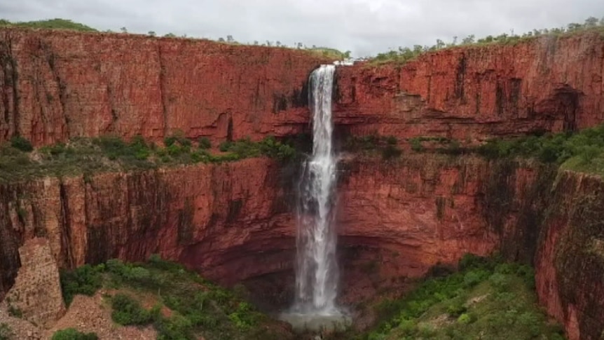 A high, wide shot of a large waterfall spilling down a red cliff face.
