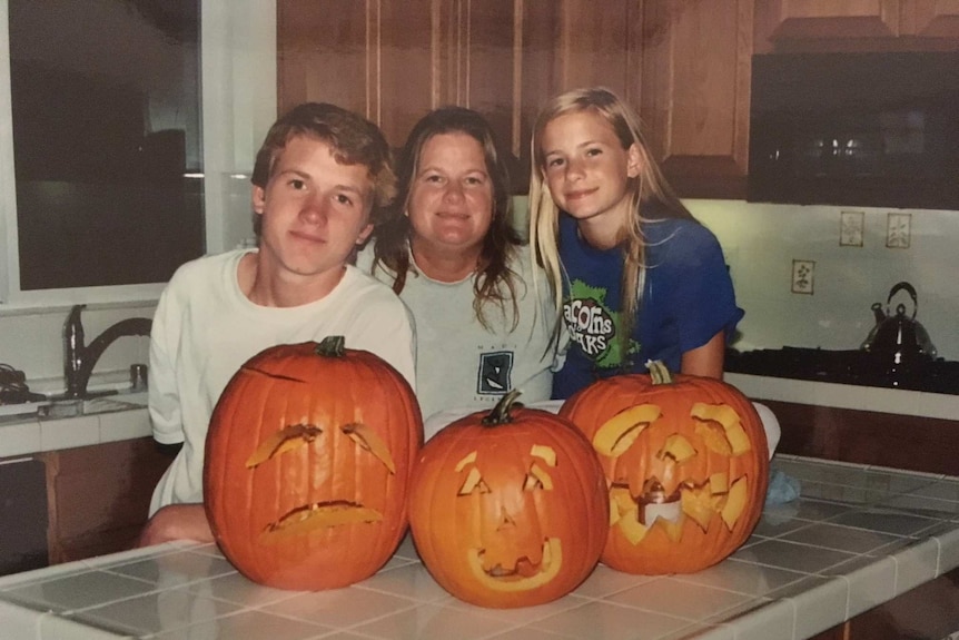 A mother with a boy and girl posing behind Halloween pumpkins