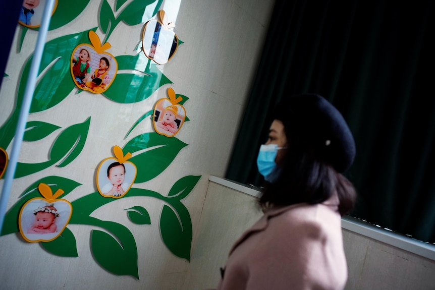 A Chinese woman in a face mask walks past images of children on a wall inside a hospital.