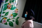 a woman in a face mask walks past a images of children on a wall inside a hospital