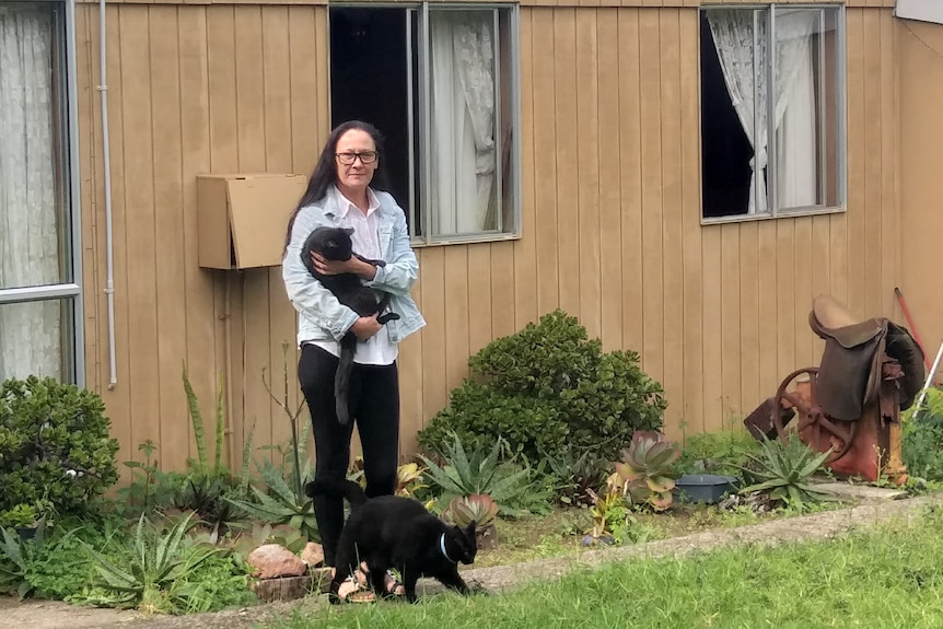 A woman stands in front of a building holding a cat.