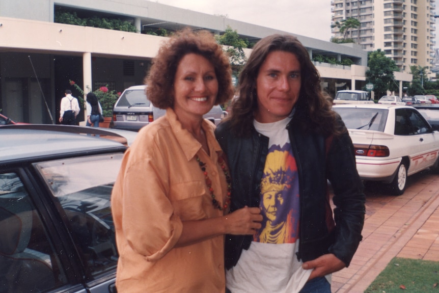 An adult mother and son stand close together on a Brisbane street after meeting for the first time. 