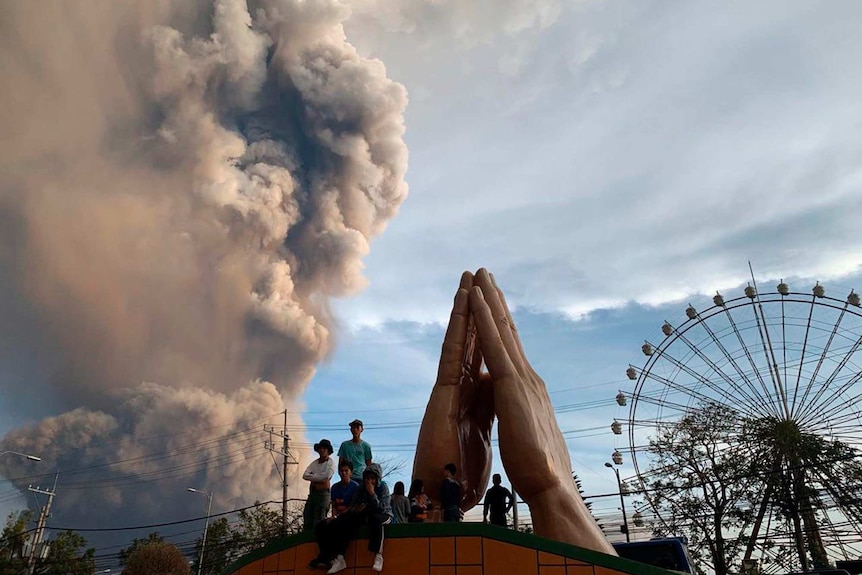 People watch in a theme park as Philippine's Taal volcano spews ash and smoke during eruption.