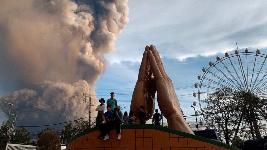 People watch in a theme park as Philippine's Taal volcano spews ash and smoke during eruption.