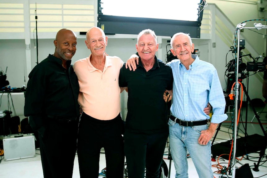 Four older men with arms around each other smiling 