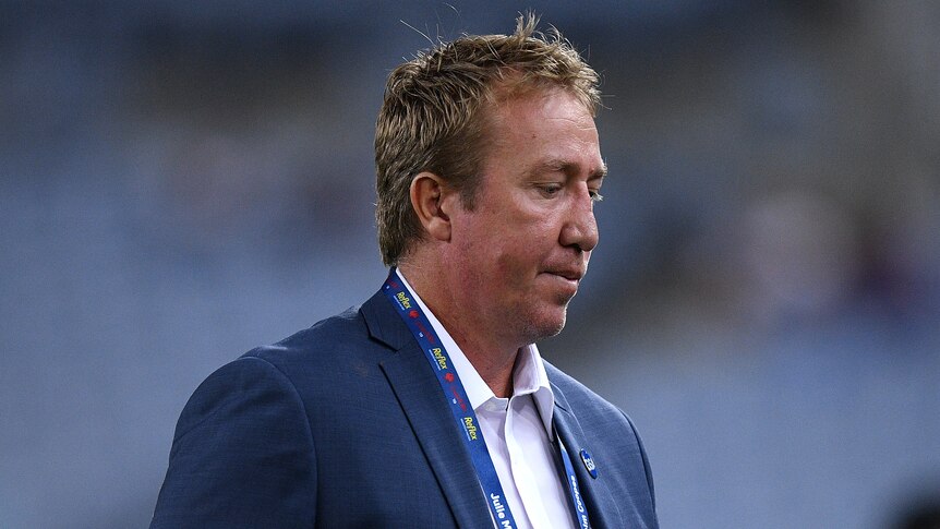 Trent Robinson looks down at the ground wearing a grey suit with open-necked white shirt