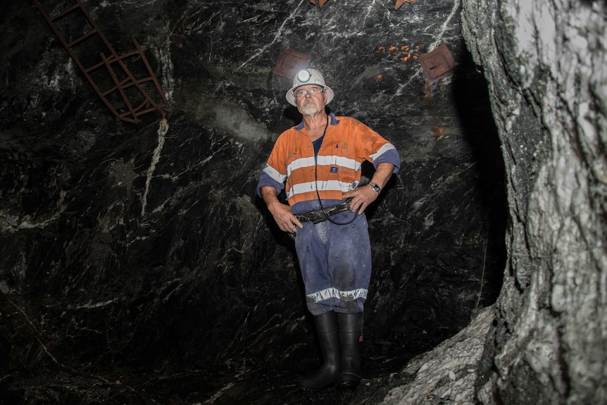 A mine worker in high-vis clothing standing in a dark cavern in an underground gold mine.