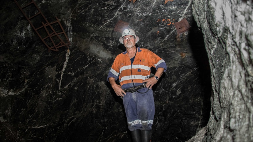 A mine worker in high-vis clothing standing in a dark cavern in an underground gold mine.