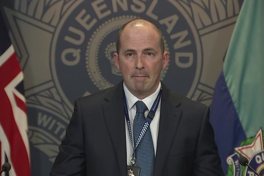 A man in a suit stands before a police logo.