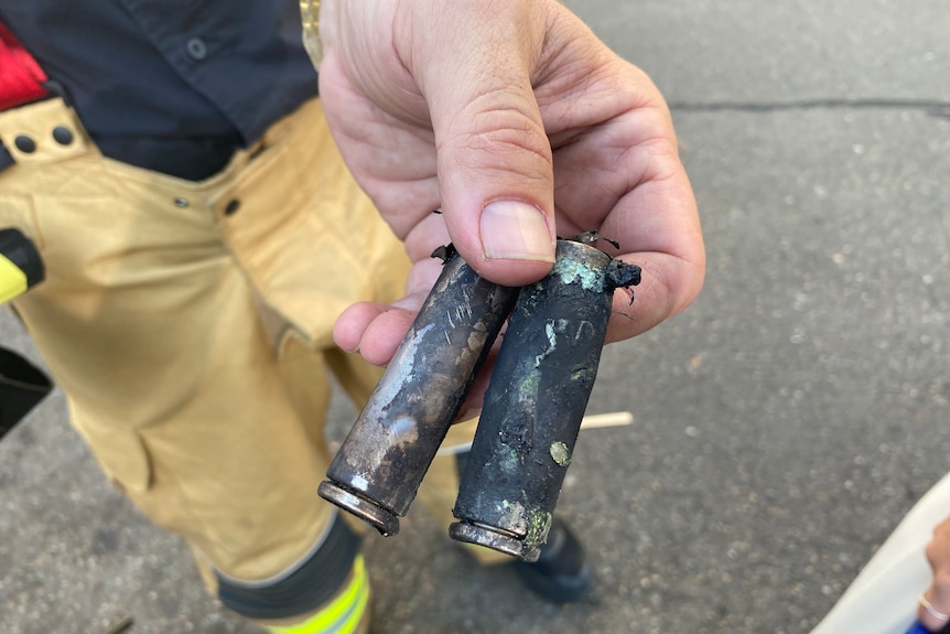 A man holds up two battery cells that are blackened and damaged after catching on fire.