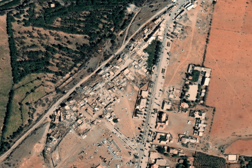 A birds' eye view shows the landscape of a village with some forest nearby, several buildings destroyed
