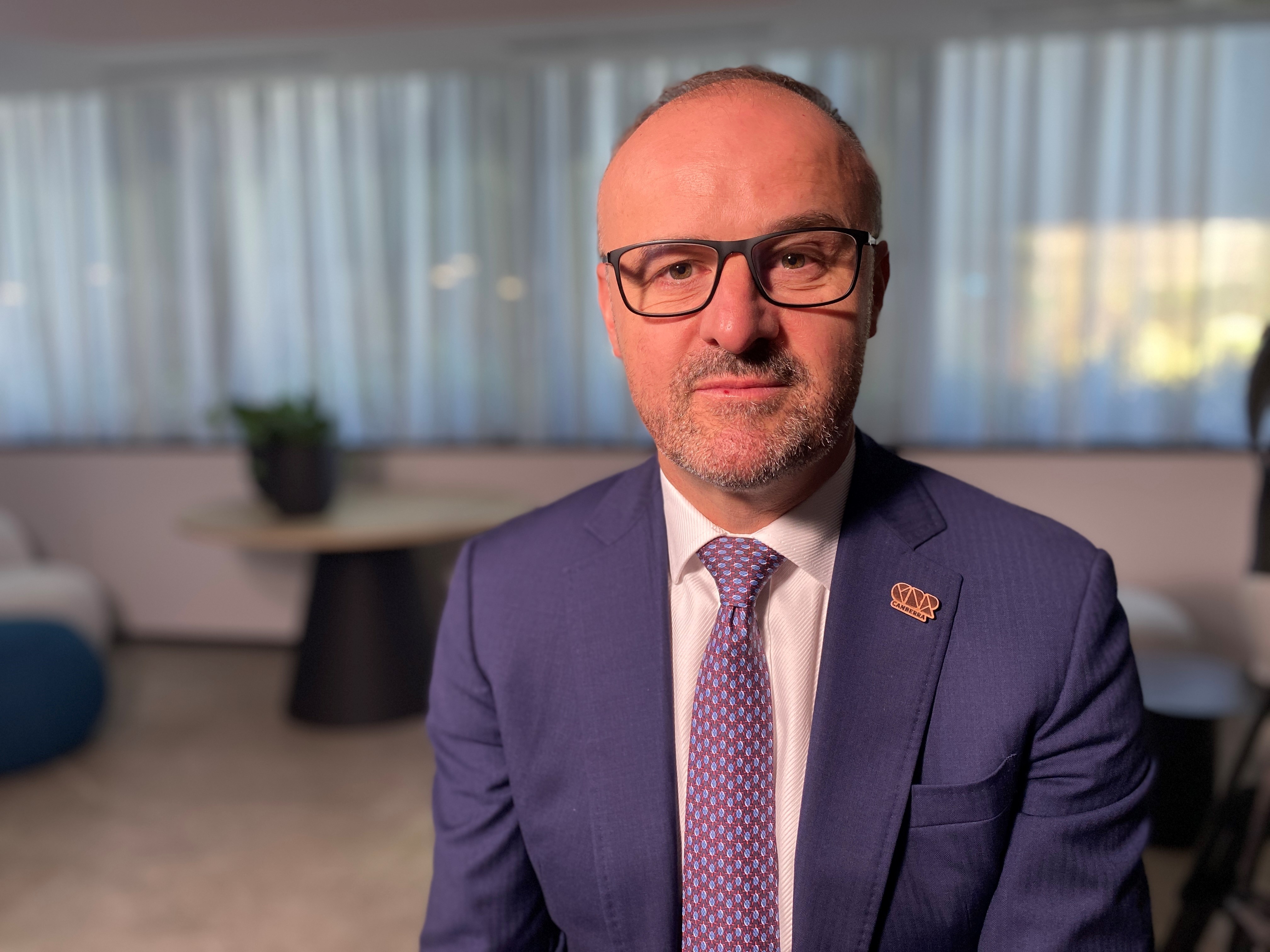 A man in a blue suit and purple tie looks serious.