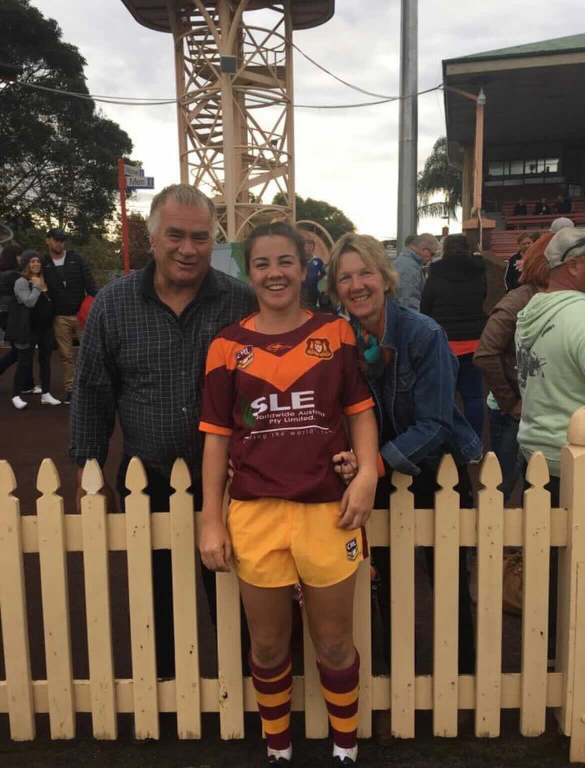 A woman in a rugby league jersey with her parents on either side of her.