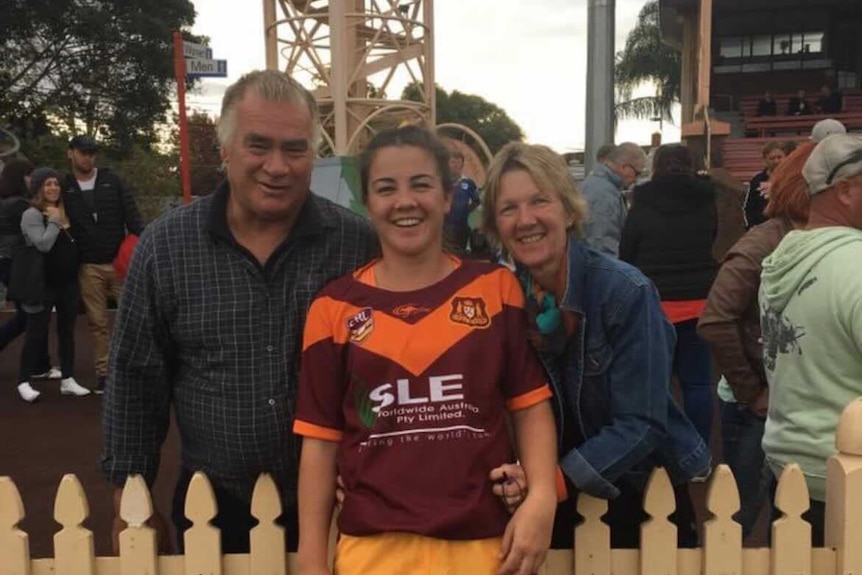 A woman in a rugby league jersey with her parents on either side of her.